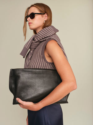 Woman holding a black clutch bag against a neutral background