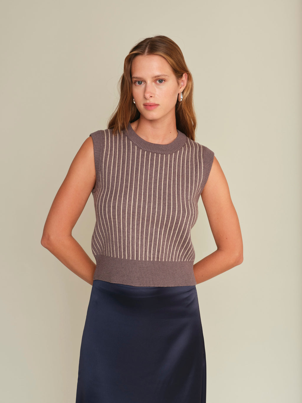 Woman wearing a sleeveless striped top and navy skirt against a beige background