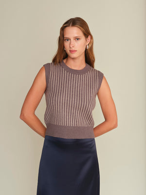 Woman wearing a sleeveless striped top and navy skirt against a beige background