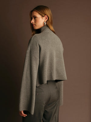 Woman wearing a gray cape over a dark outfit against a brown background