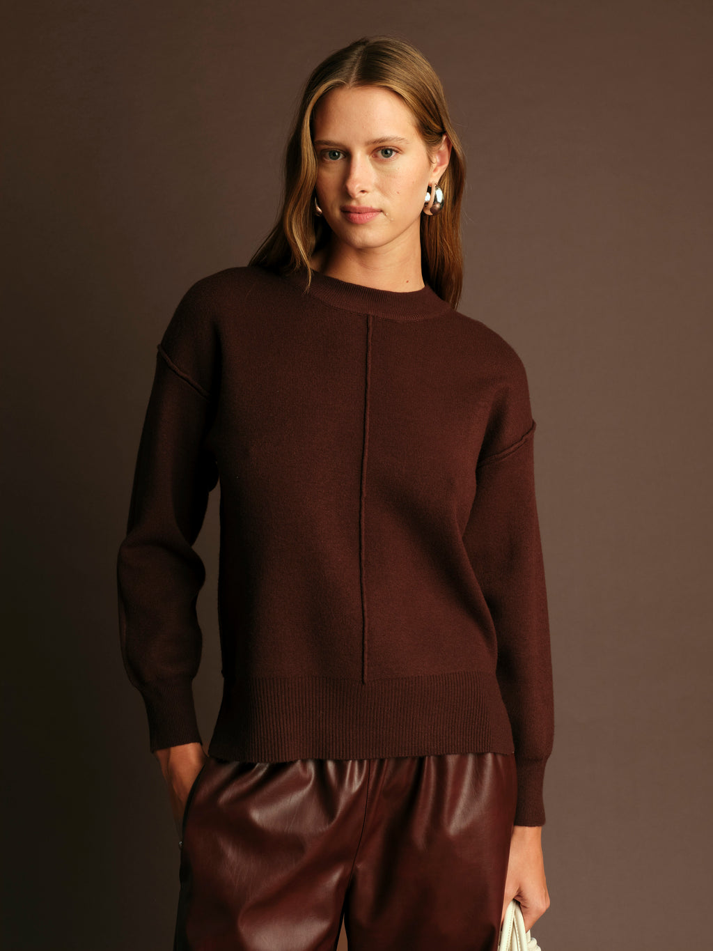 Woman wearing a brown sweater and pants against a dark background