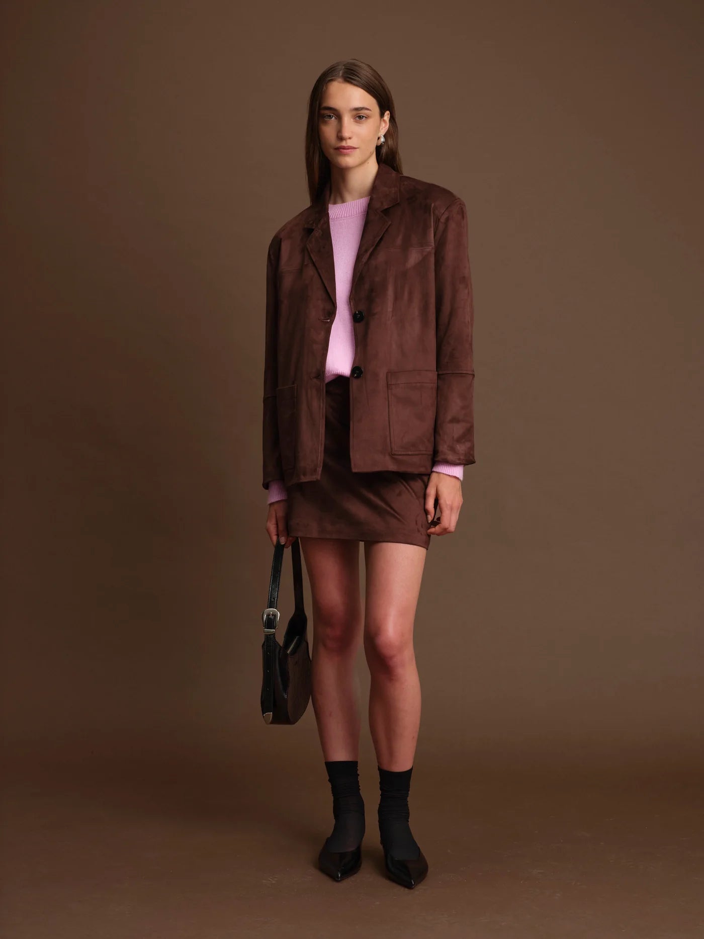 Woman wearing a brown outfit with a pink top against a brown background