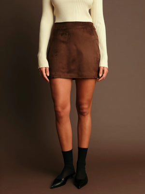 Person wearing a brown suede skirt with a plain background