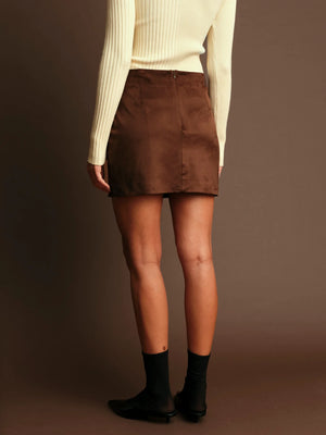 Person wearing a brown skirt and white sweater against a brown background