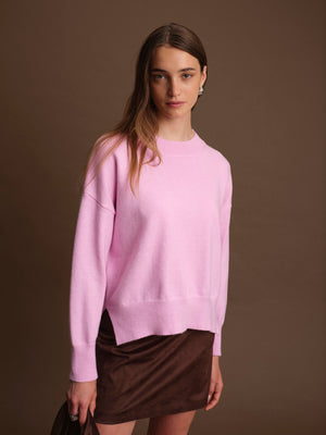 Woman wearing a pink sweater over a brown skirt against a brown background