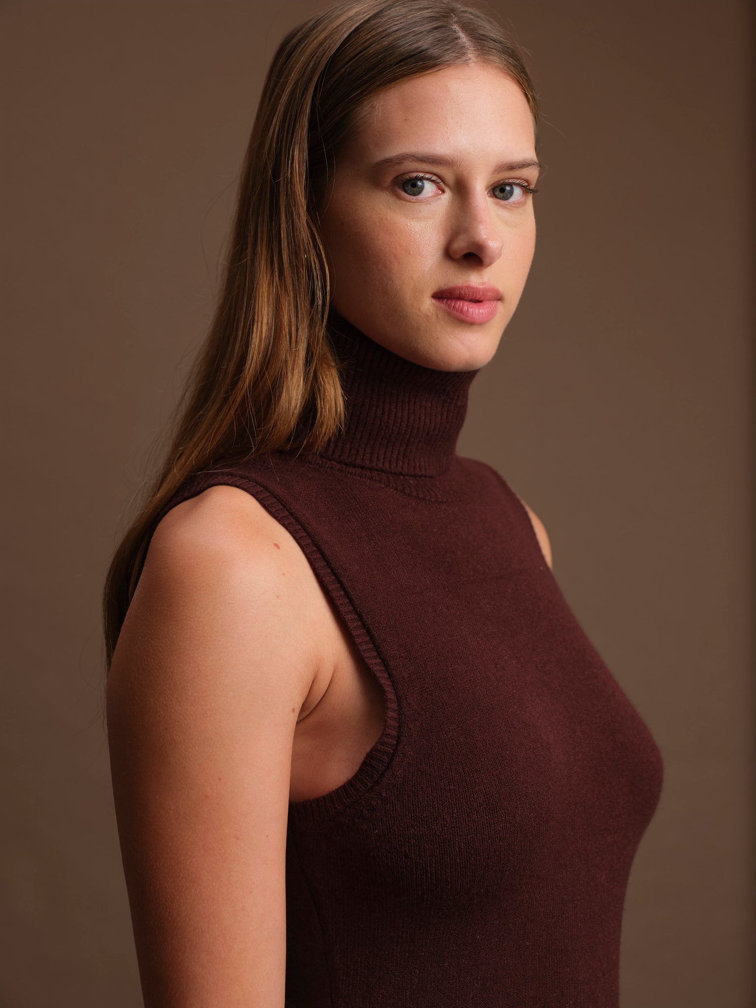Woman wearing a brown sleeveless turtleneck against a brown background