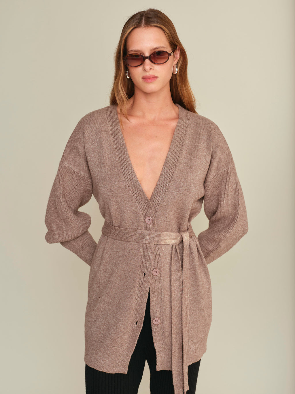 Woman wearing a brown cardigan with a belt on a plain background