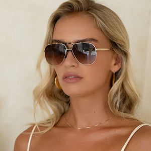 Woman wearing gold aviator sunglasses and hoop earrings with a neutral background