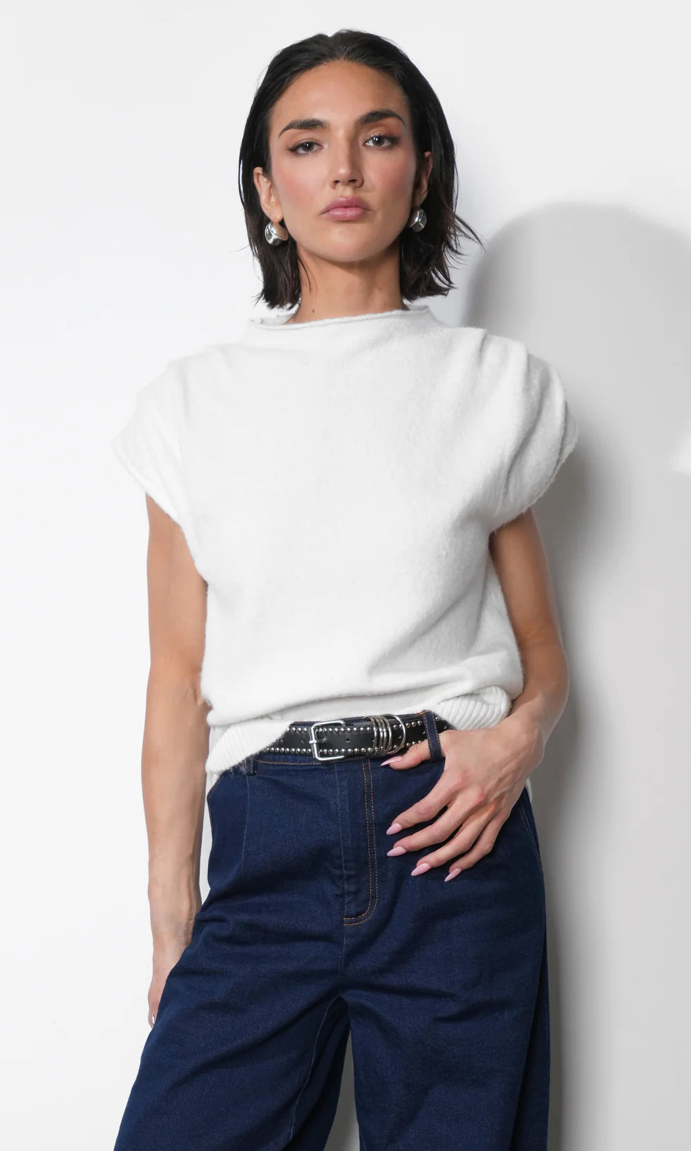 Woman wearing a white sweater and blue jeans against a plain background