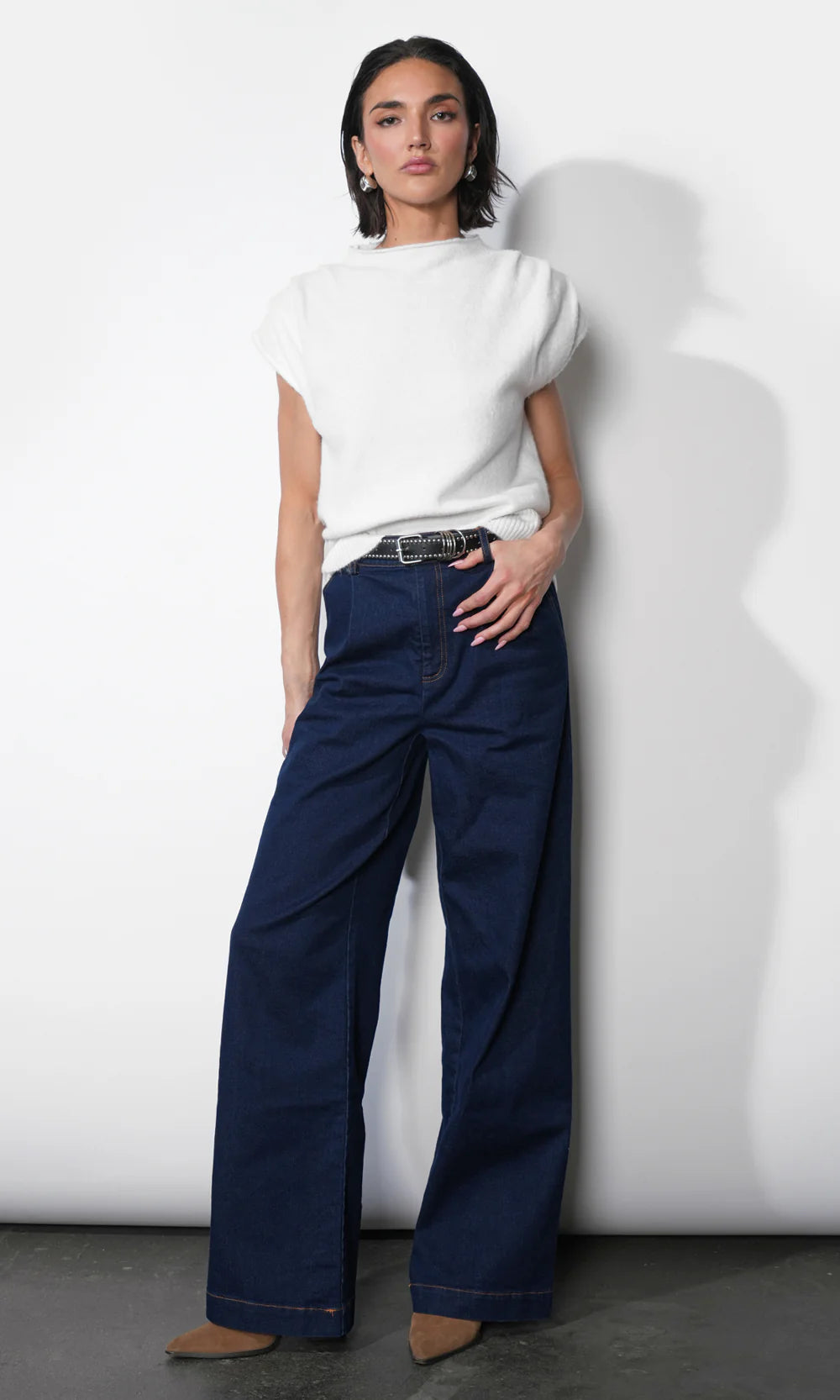 Woman wearing a white top and blue jeans against a white background