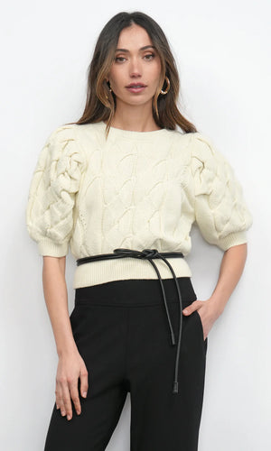 Woman wearing a cream knitted top and black pants against a white background