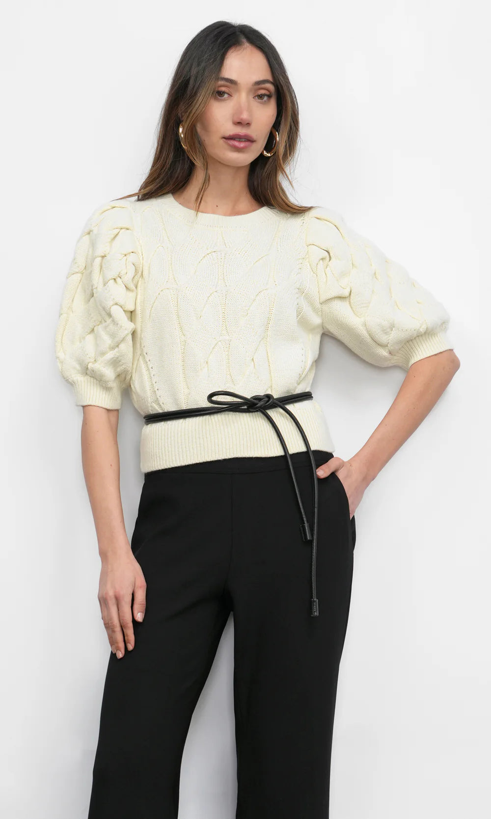 Woman wearing a cream knitted top and black pants on a white background