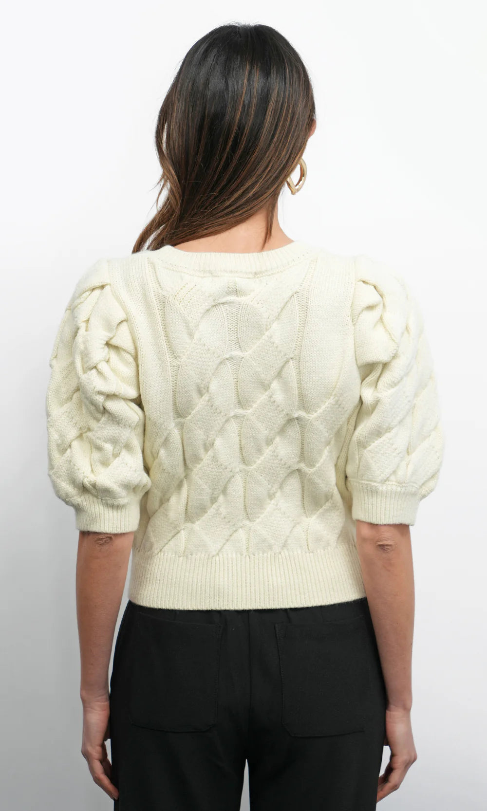 Person wearing a cream-colored cable knit sweater with puff sleeves on a white background