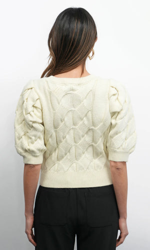 Person wearing a cream-colored cable knit sweater with puff sleeves on a white background