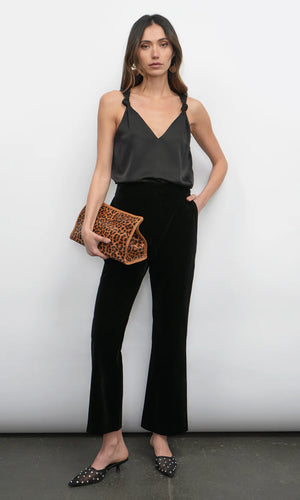 Woman wearing a black sleeveless top and black pants, holding a leopard print clutch against a white background.