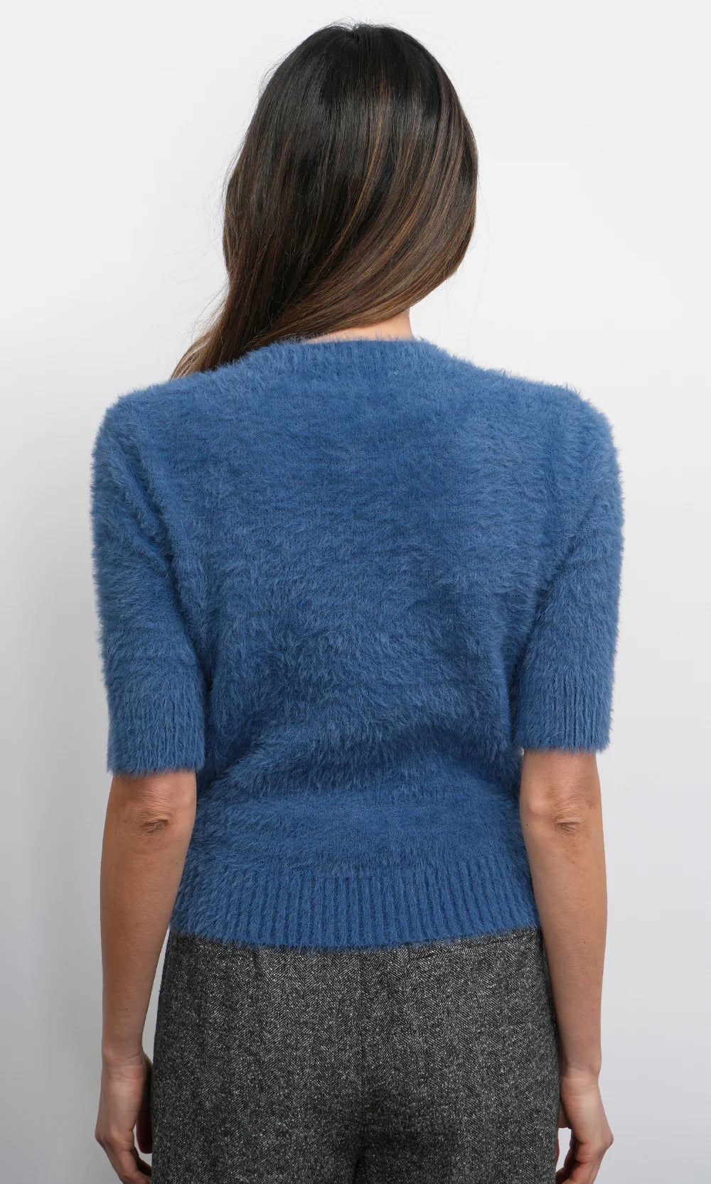 Person wearing a blue fuzzy sweater with gray pants on a white background
