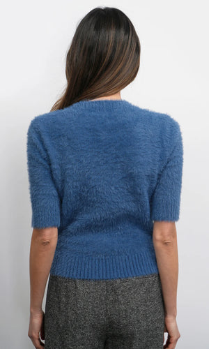 Person wearing a blue fuzzy sweater with gray pants on a white background