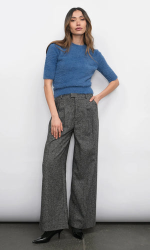 Woman wearing a blue sweater and gray wide-leg pants against a white background