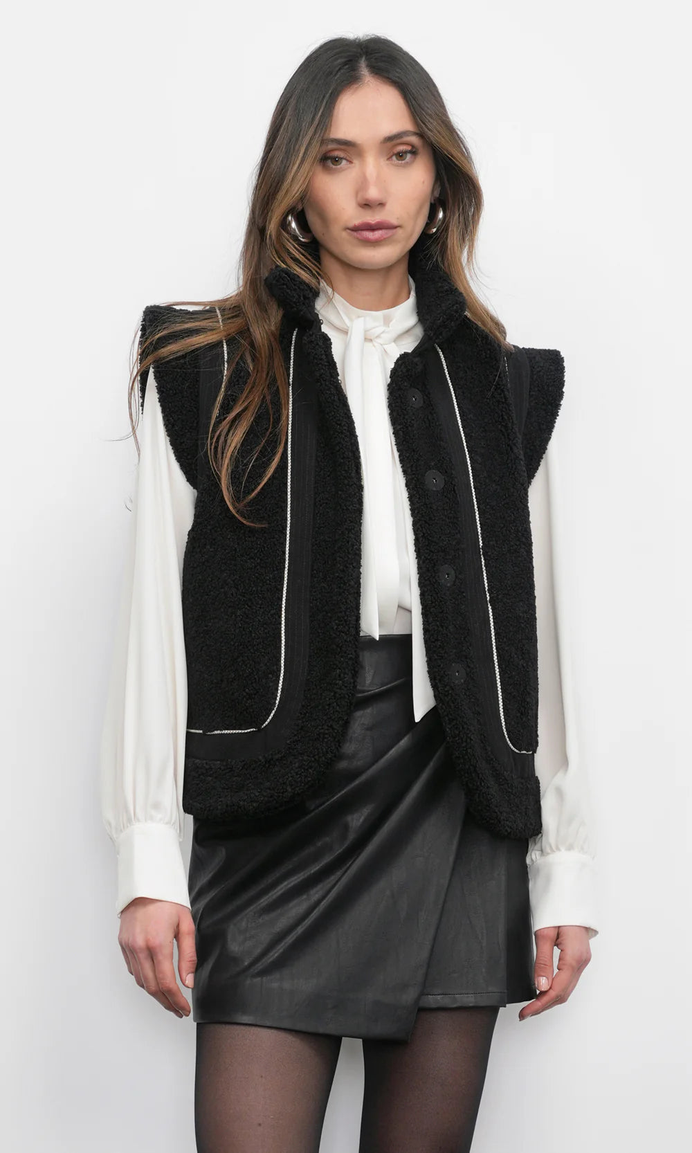 Woman wearing a black vest over a white blouse and black skirt on a white background