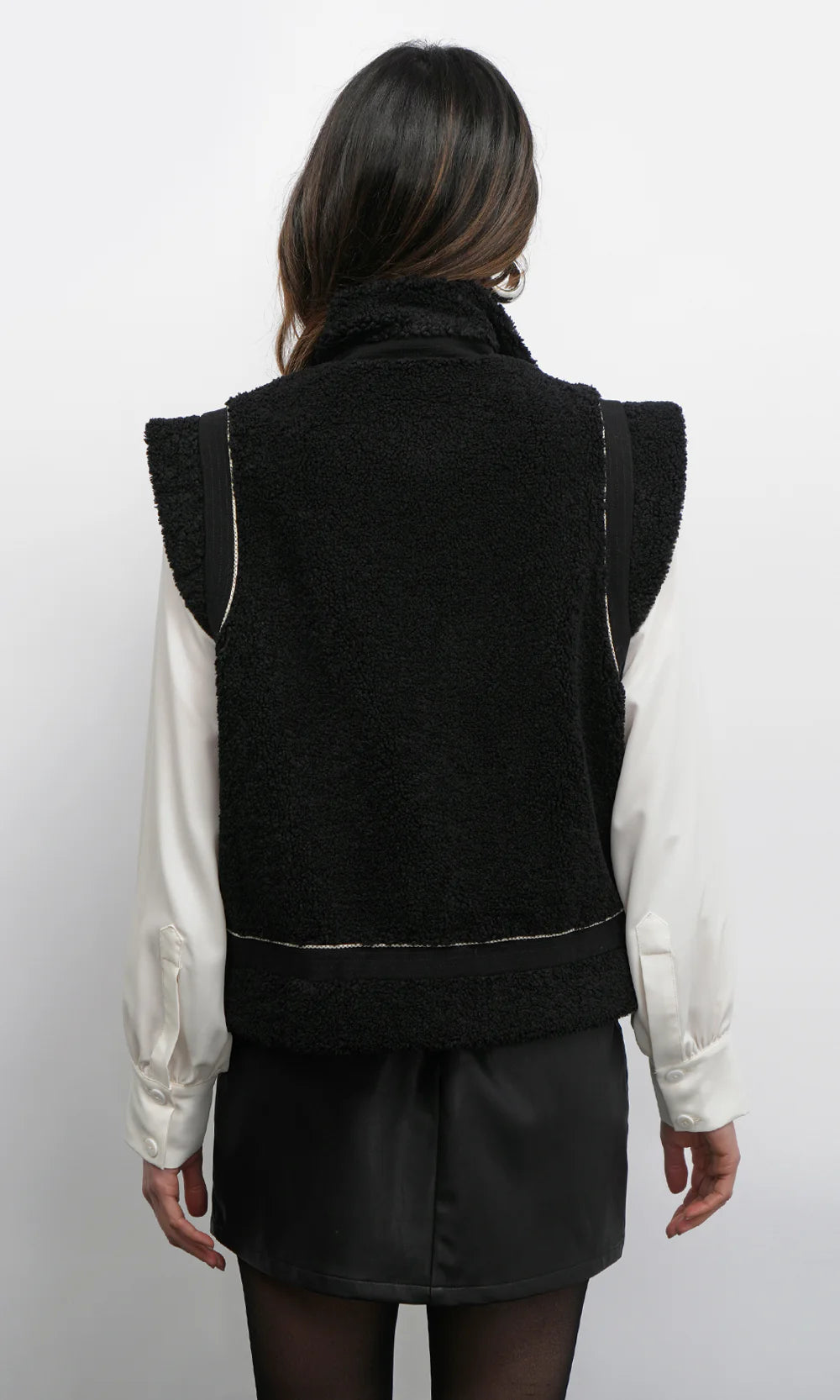 Person wearing a black knitted vest over a white shirt on a plain background