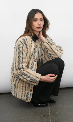 Woman wearing a patterned beige coat sitting on a white surface.