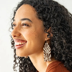 Woman with curly hair wearing a brown top and gold earrings on a white background