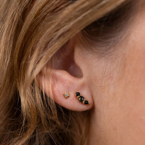 Close-up of an ear wearing two gold earrings with black stones and a star detail.