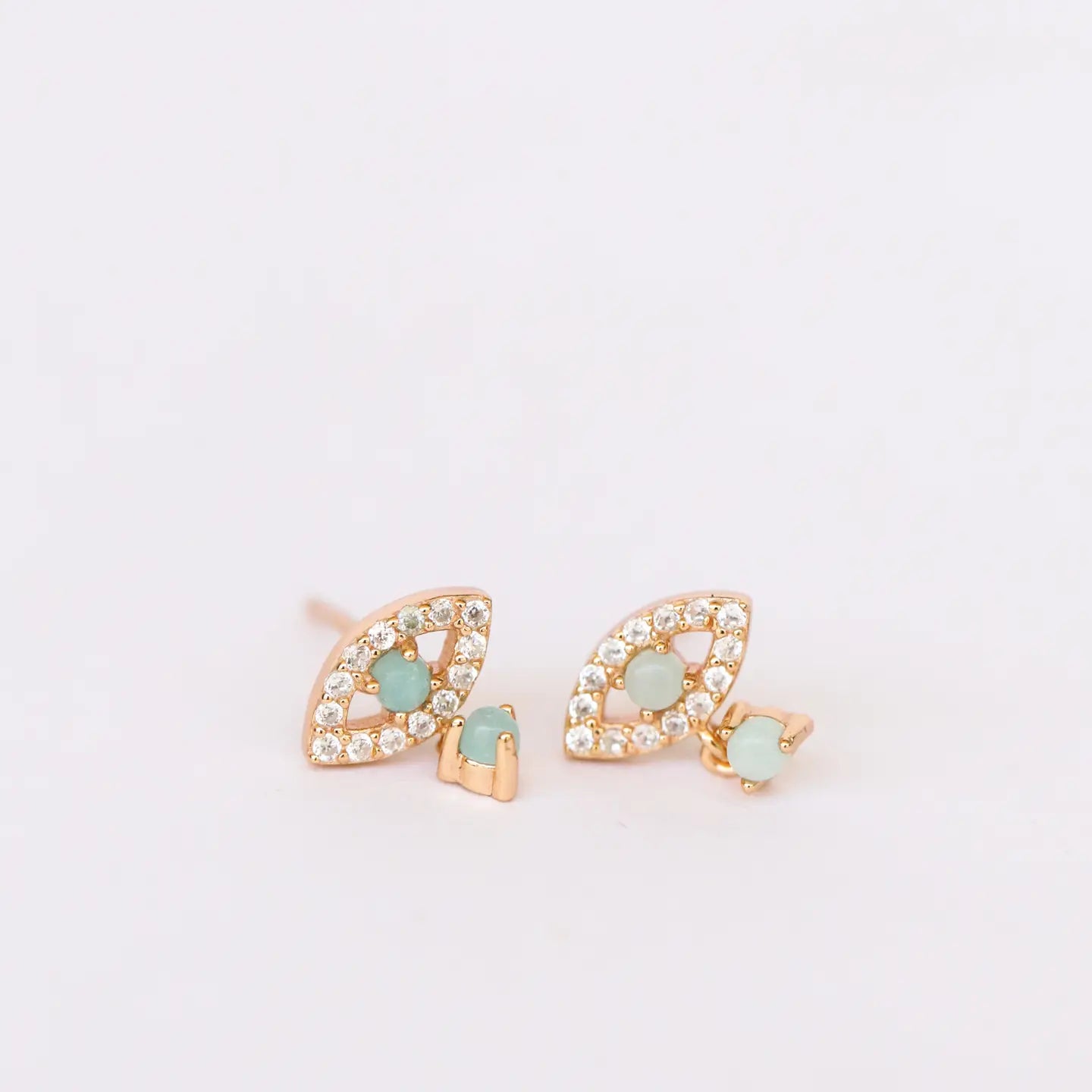 Pair of gold earrings with green gemstones on a light pink background