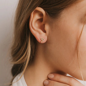 Close-up of a woman's ear wearing a gold earring with a diamond.