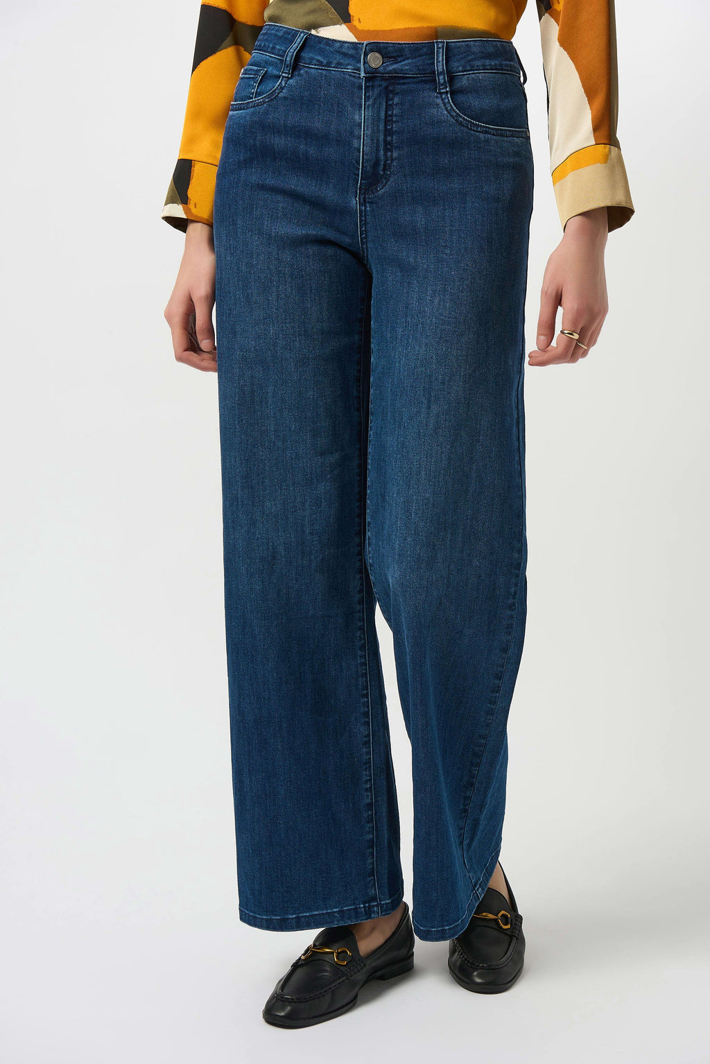 Person wearing blue jeans with a multicolored shirt and black loafers on a white background