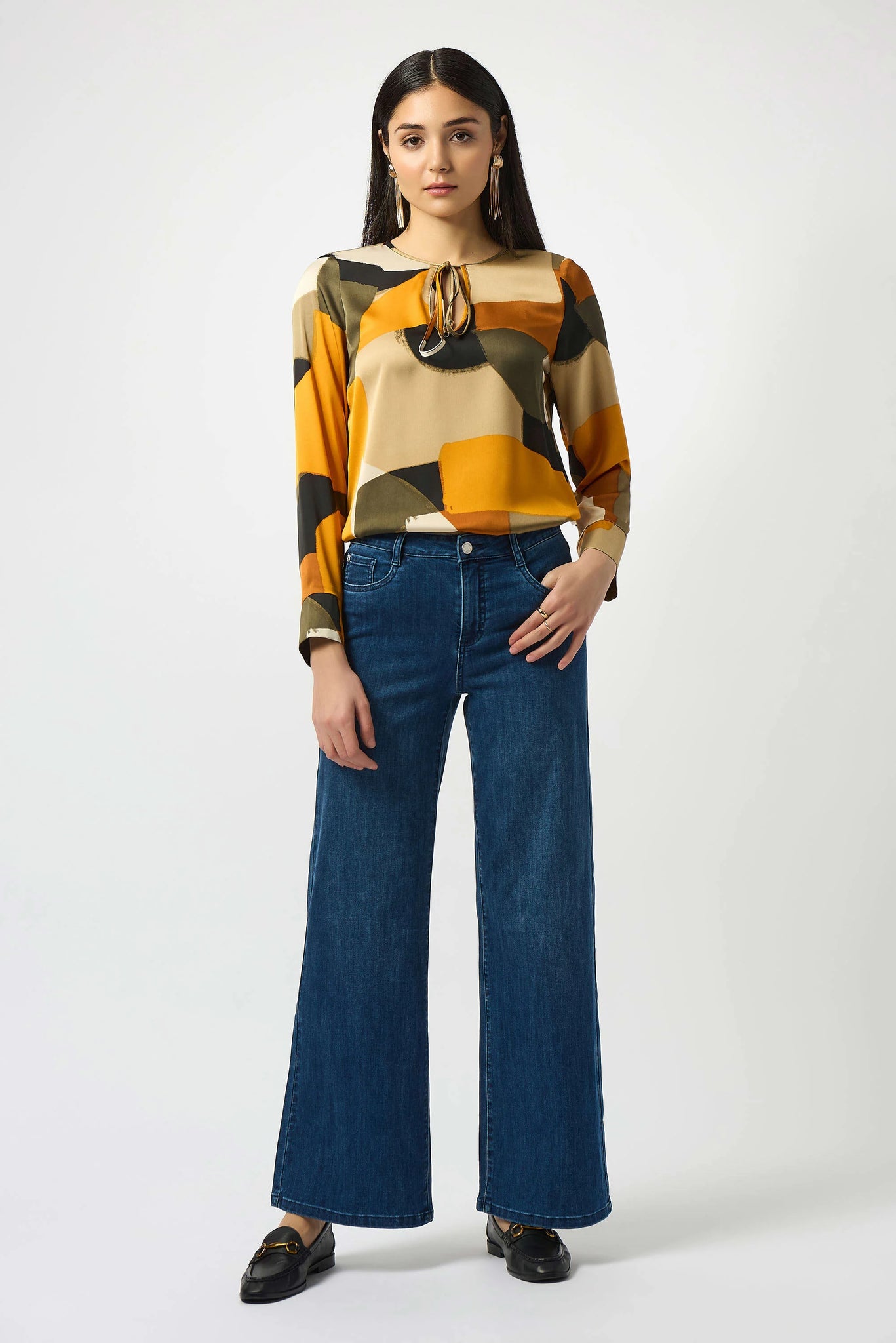 Woman wearing a patterned top and blue jeans on a white background