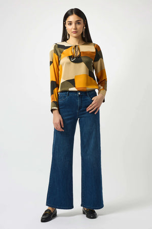 Woman wearing a patterned top and blue jeans on a white background