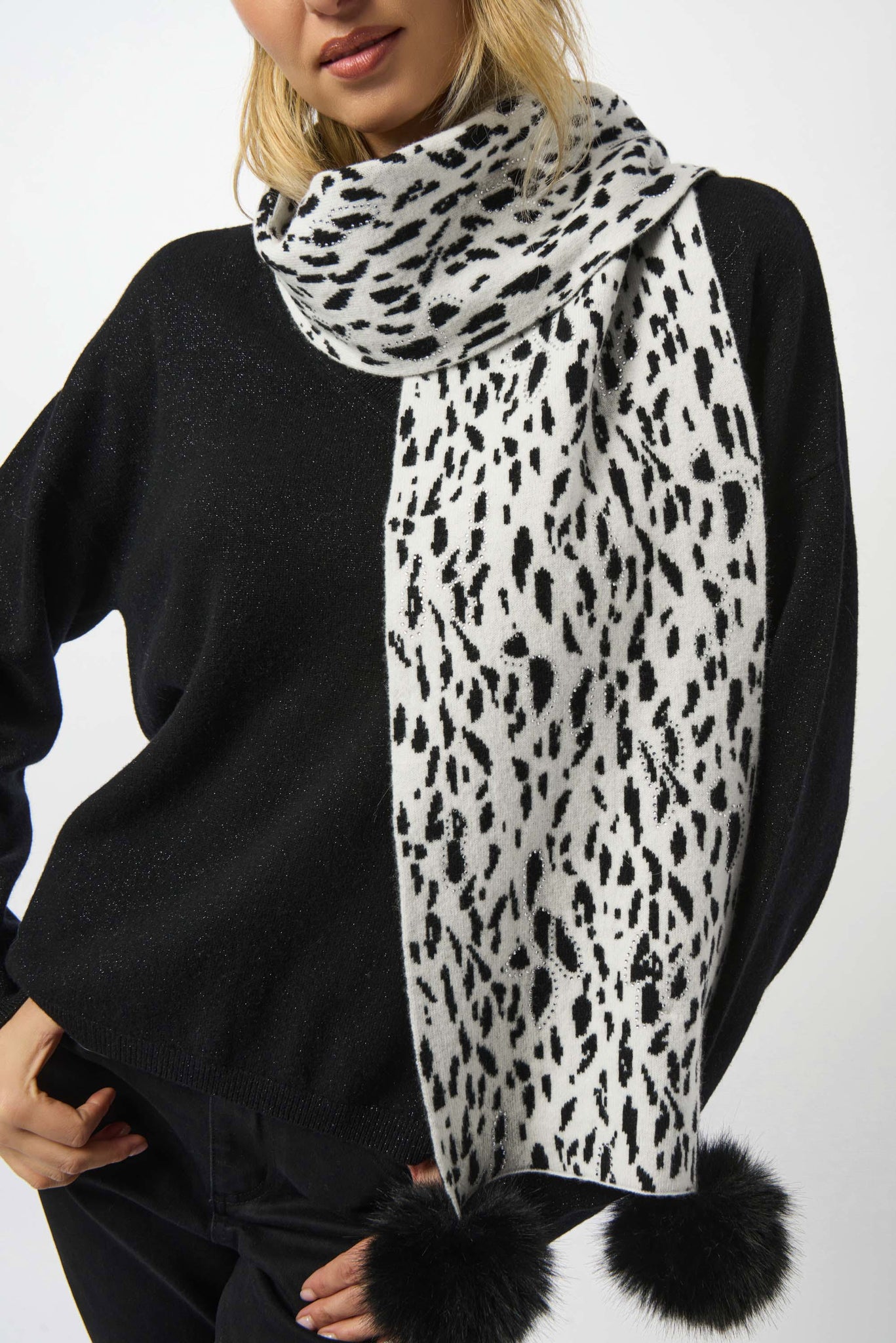 Person wearing a black sweater and a leopard print scarf with pom-poms on a white background