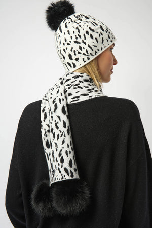Person wearing a black and white leopard print scarf with pom-poms on a plain background