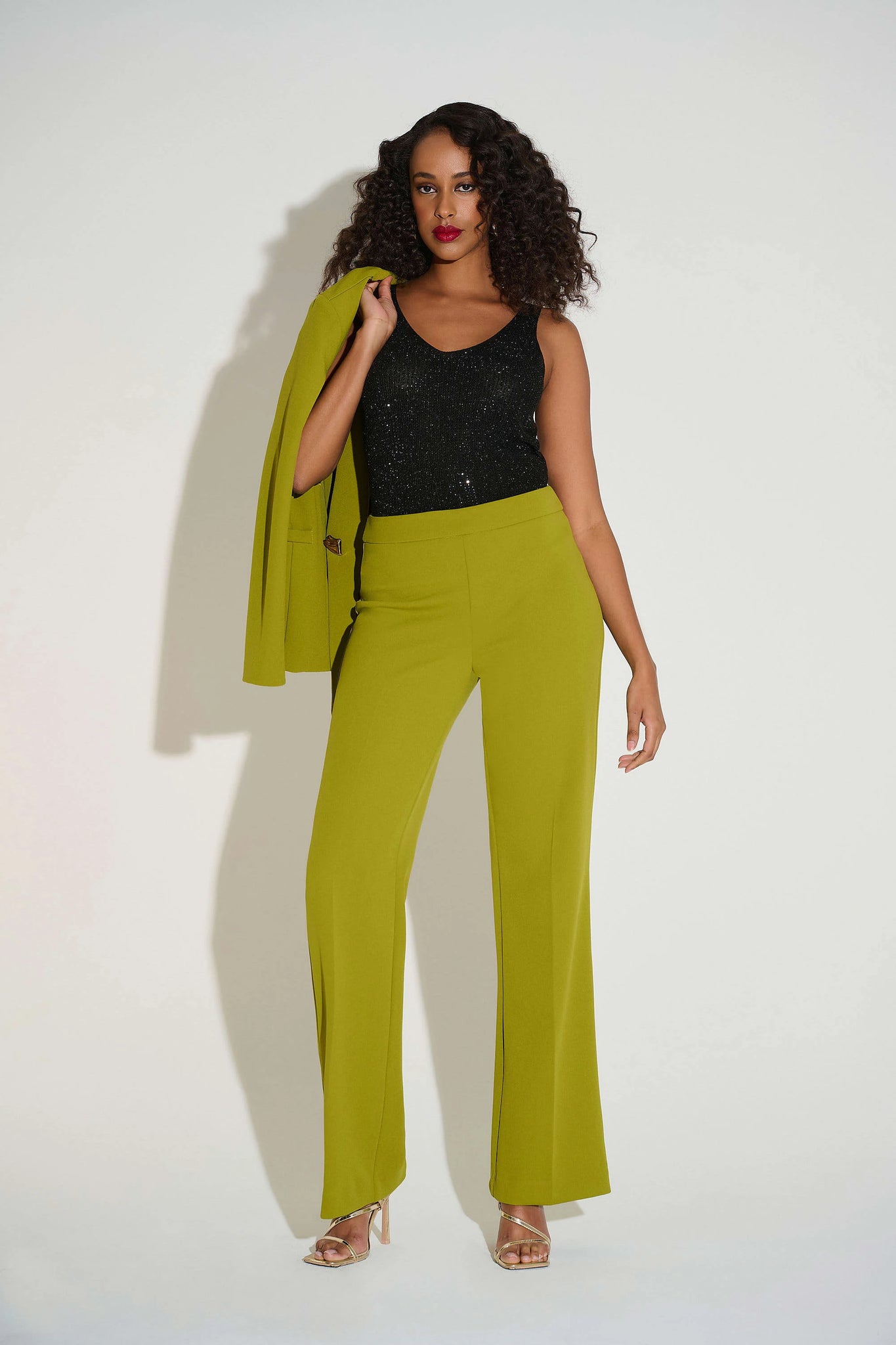 Woman wearing a black top and green pants with a green jacket on a white background