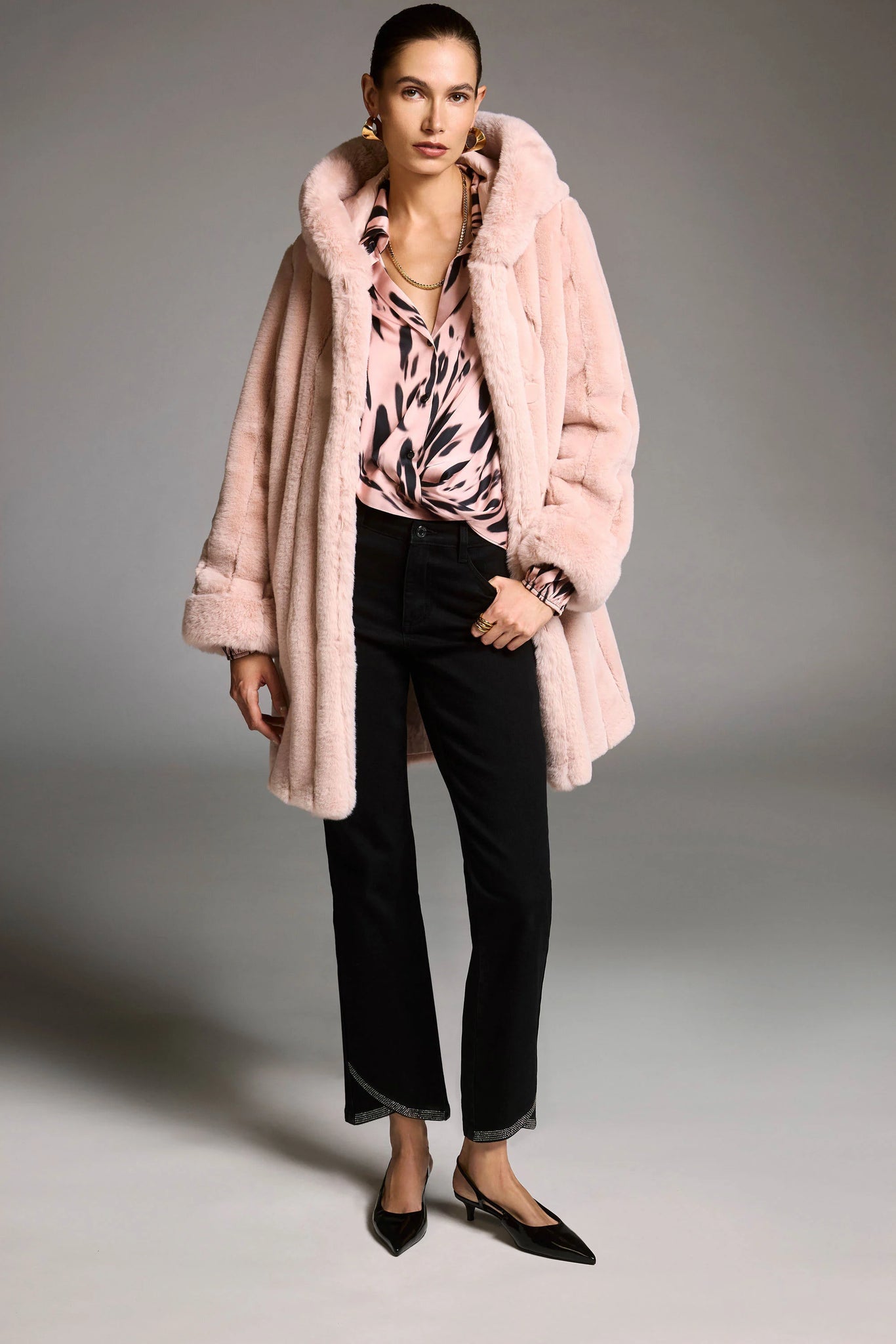 Woman wearing a pink coat, patterned top, and black pants on a gray background