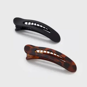 Two hair clips, one black and one tortoiseshell, on a light gray background.