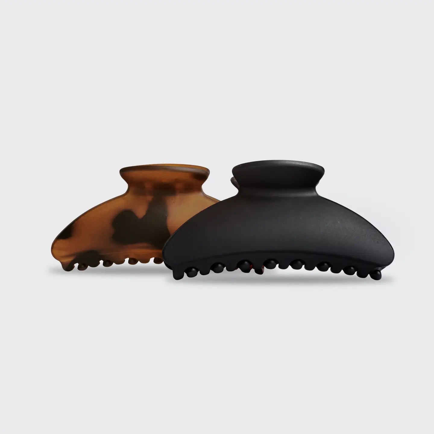 Two hair clips, one tortoiseshell and one black, on a light gray background.