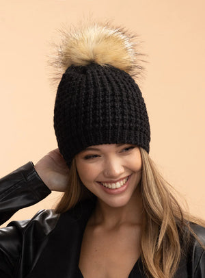 Woman wearing a black knit beanie with a fur pom-pom against a beige background