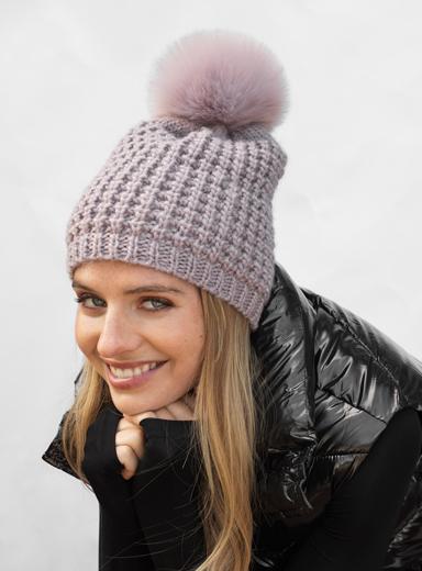 Woman wearing a knitted beanie with a pink pom-pom against a white background