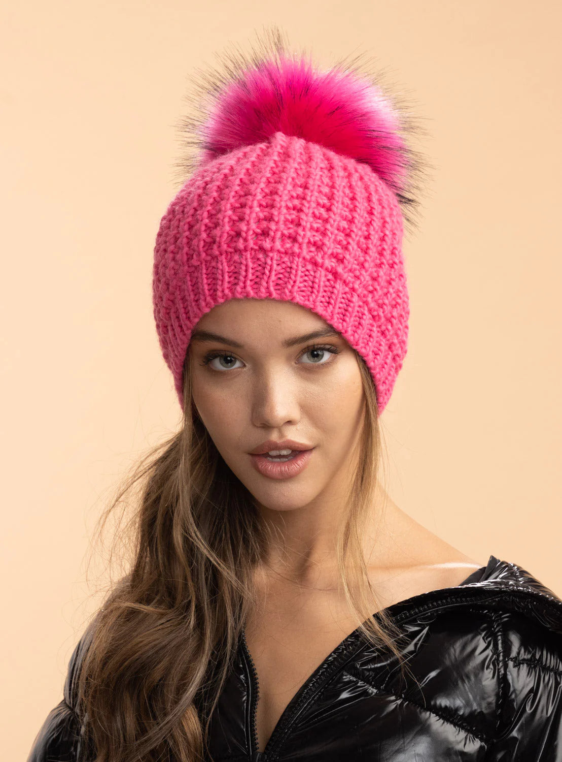 Woman wearing a pink knit beanie with a large fur pom-pom on a beige background