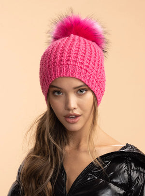Woman wearing a pink knit beanie with a large fur pom-pom on a beige background
