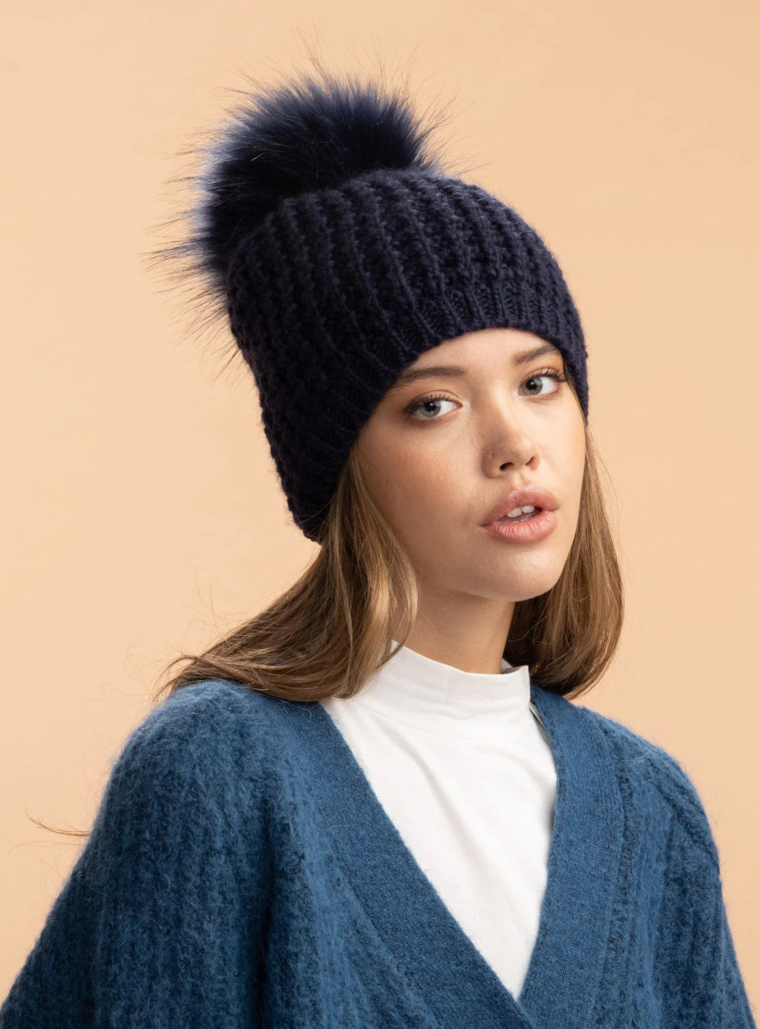 Woman wearing a navy knit beanie with a pom-pom against a beige background