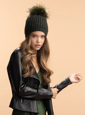 Woman wearing a black knit beanie with a pom-pom and black leather jacket on a beige background