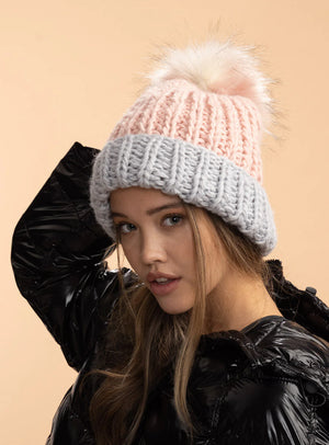 Woman wearing a two-tone knit beanie with a fluffy pom-pom on a beige background