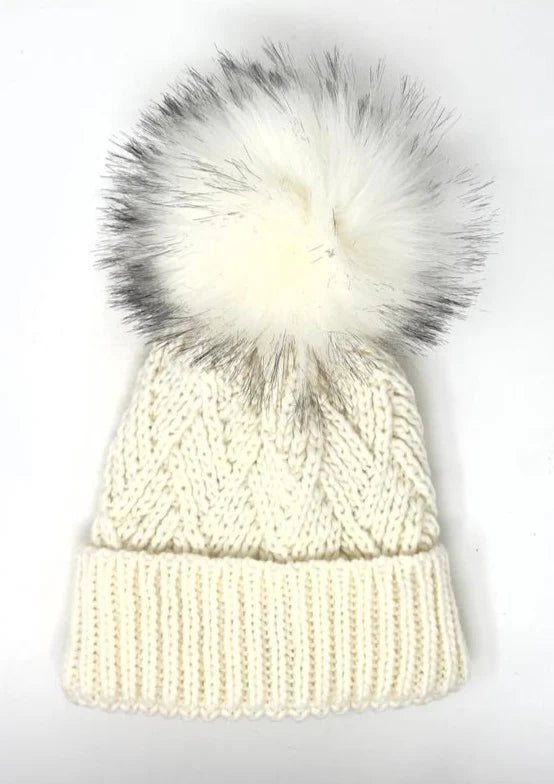 White knit beanie with a large faux fur pom-pom on a white background