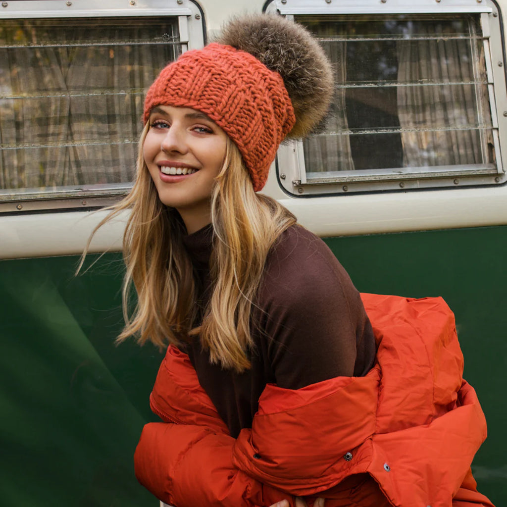 Woman wearing an orange knit beanie and red jacket standing in front of a green vehicle.