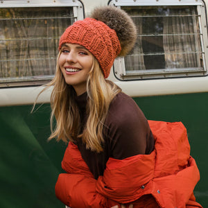 Woman wearing an orange knit beanie and red jacket standing in front of a green vehicle.