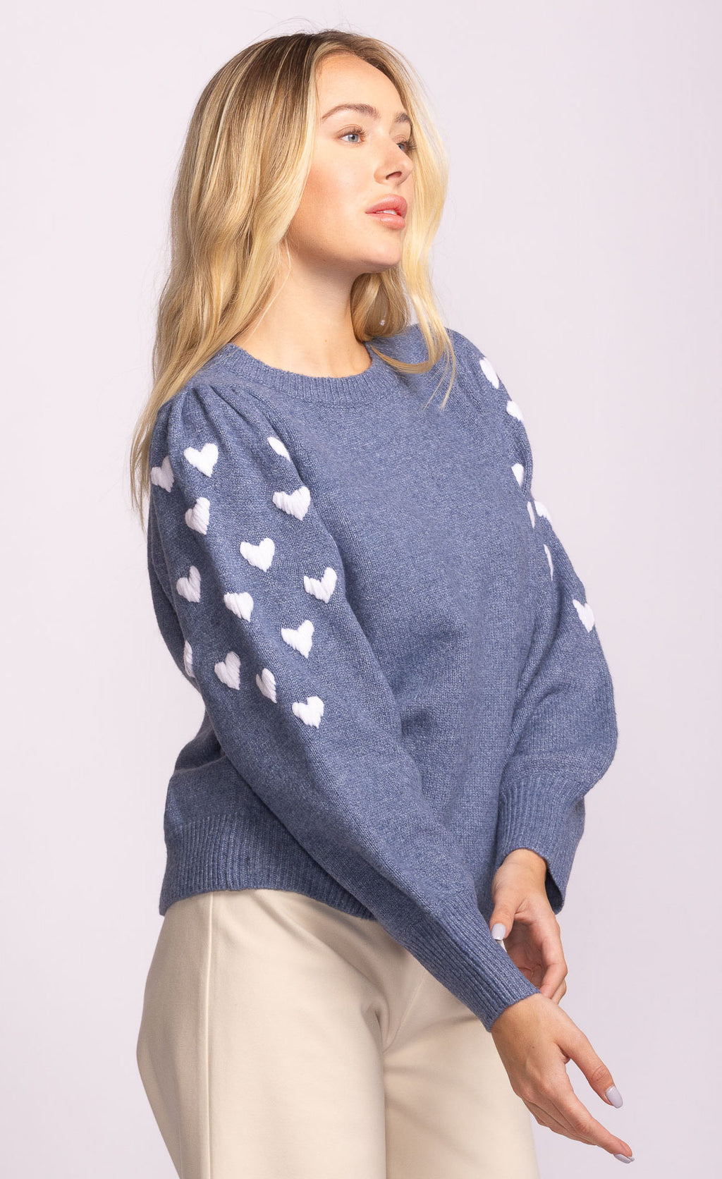 Woman wearing a blue sweater with white heart patterns on a plain background