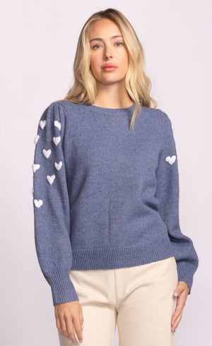 Woman wearing a blue sweater with white heart patterns on a light pink background